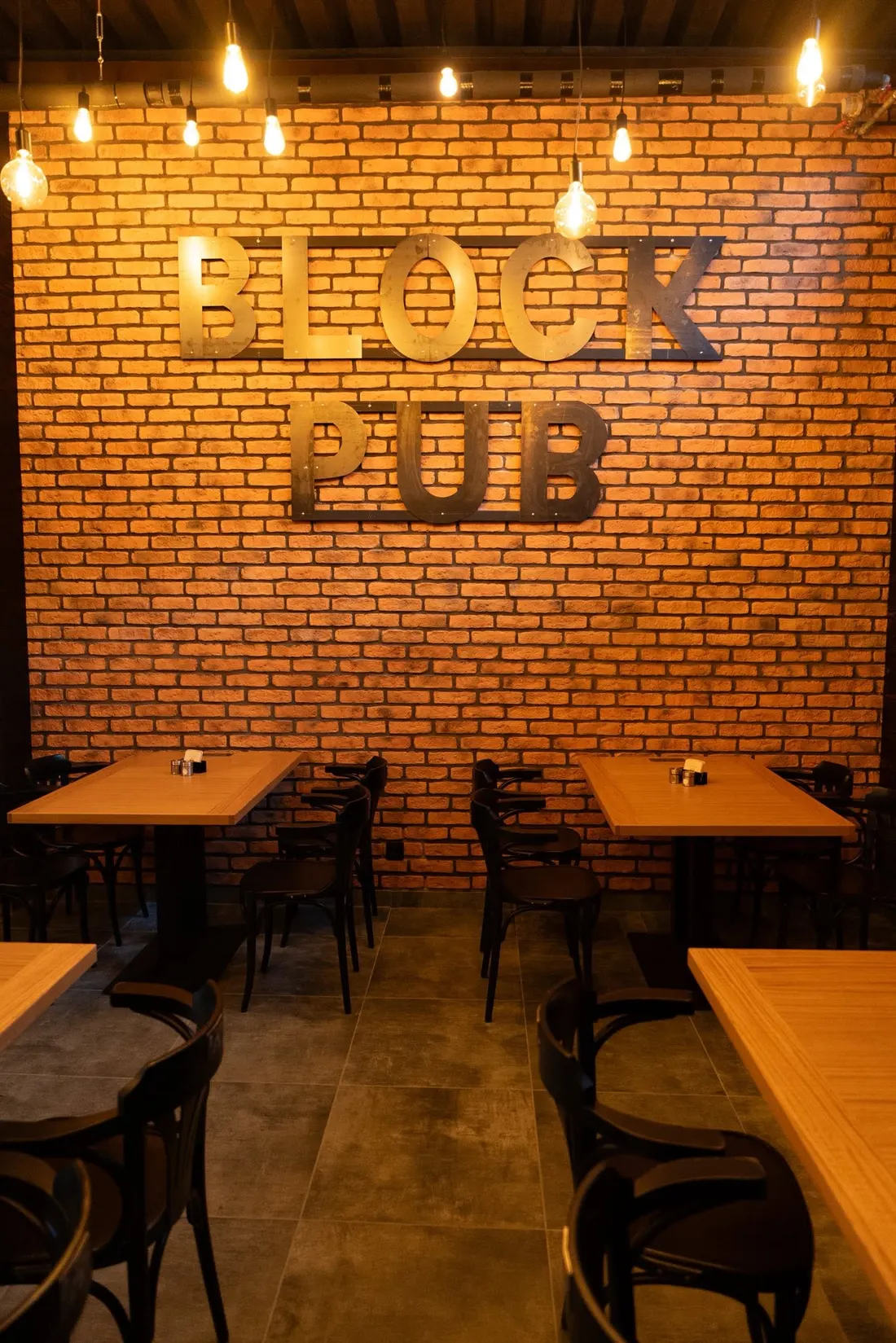 Nápis BLOCK PUB z kovových písmen na tehlovej stene
